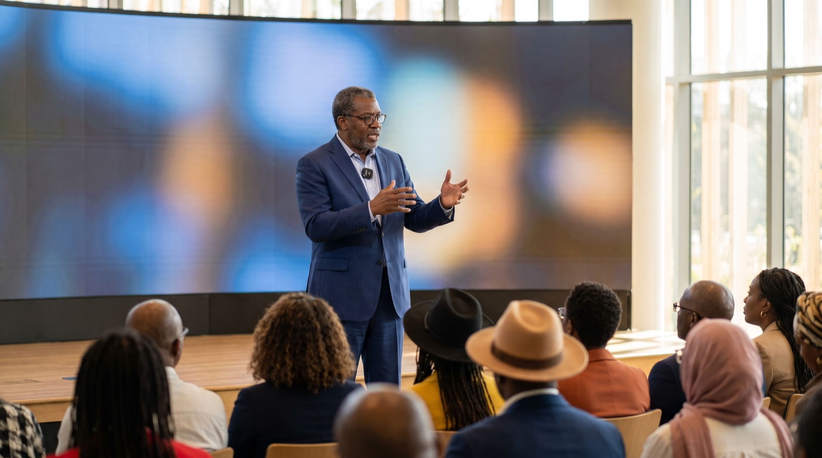 A speaker presents on a stage (Sample)